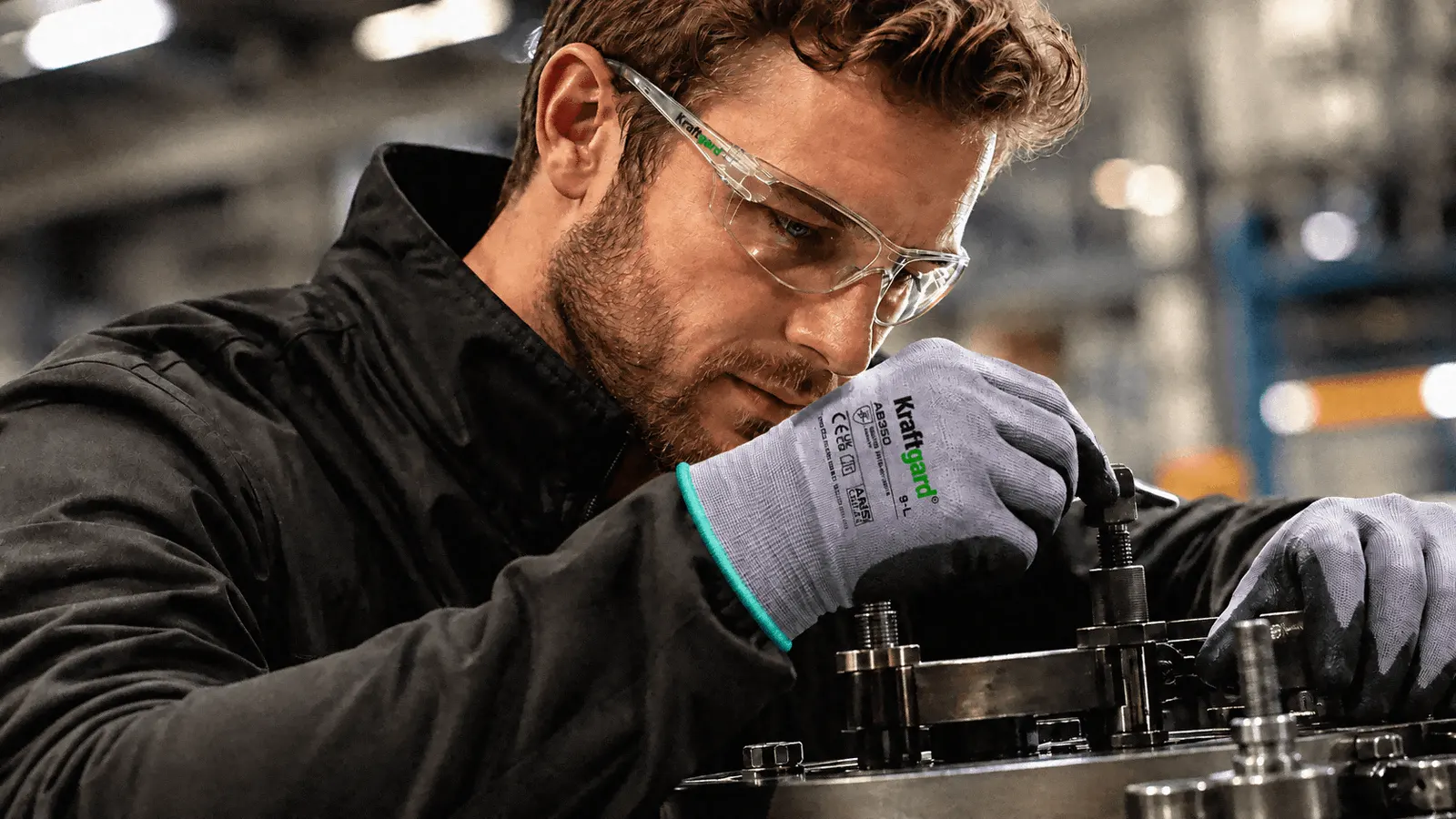 Industrial worker wearing Kraftgard safety glasses and gloves assembling a machine part.